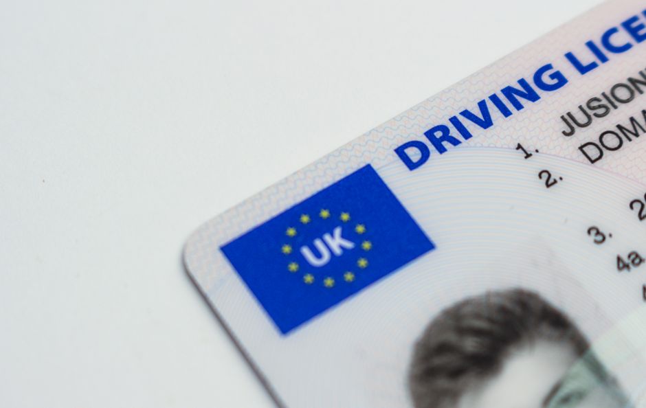 Close-up of the corner of a UK driving licence on a white surface, showing the blue UK flag panel and the start of a photograph