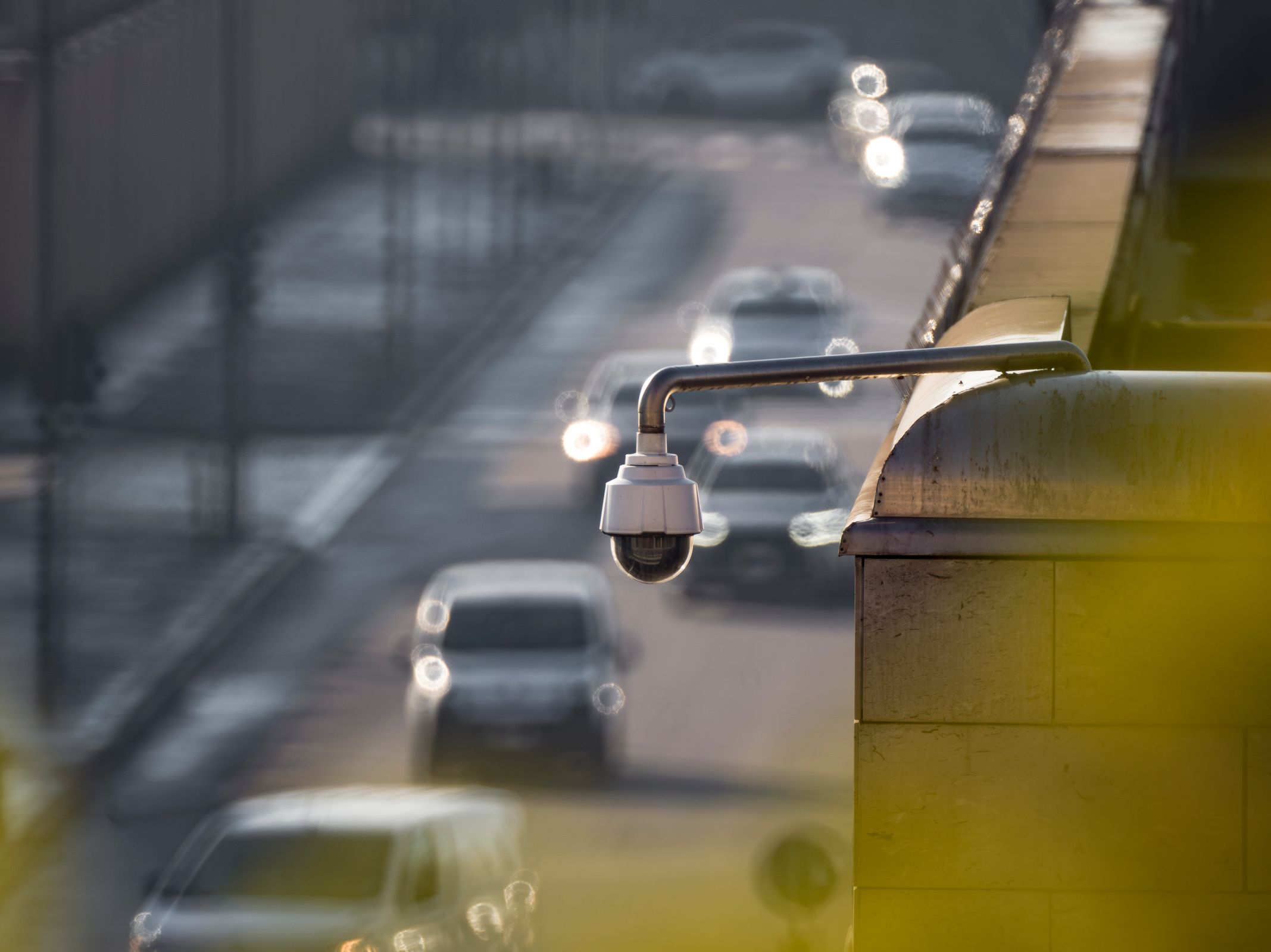 Eine Dome-Überwachungskamera an einer Überführung beobachtet eine belebte Straße mit Verkehr darunter.