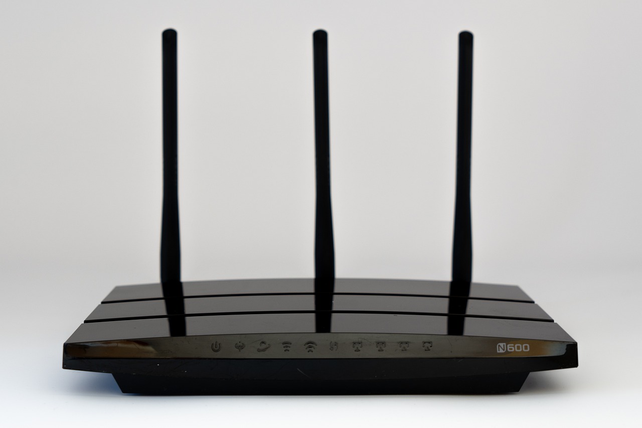 A black Wi-Fi router with three upright antennas on a white background, its status icons printed along the front edge. This is the device that sees where your traffic goes, not what is inside it.