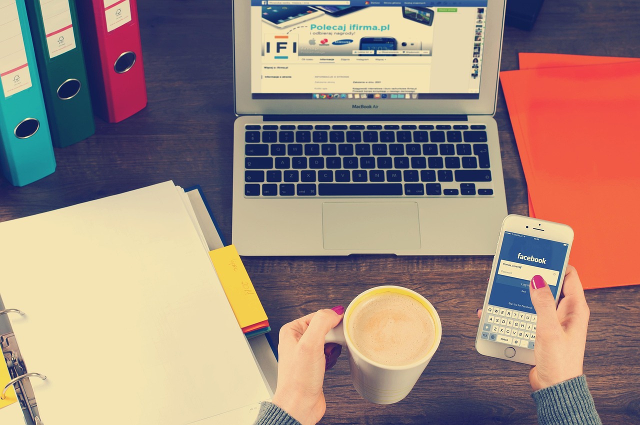 A laptop, smartphone and coffee on a desk with social media open