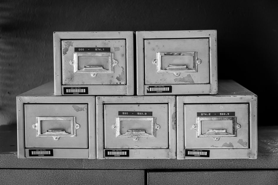 Five metal card-index drawers stacked in a pyramid, photographed in black and white, their labels showing numeric ranges and small barcodes