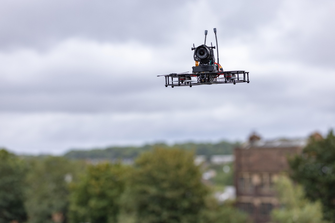 Eine mit einer Kamera ausgestattete Quadrokopter-Drohne im Flug über einer Stadt unter bewölktem Himmel