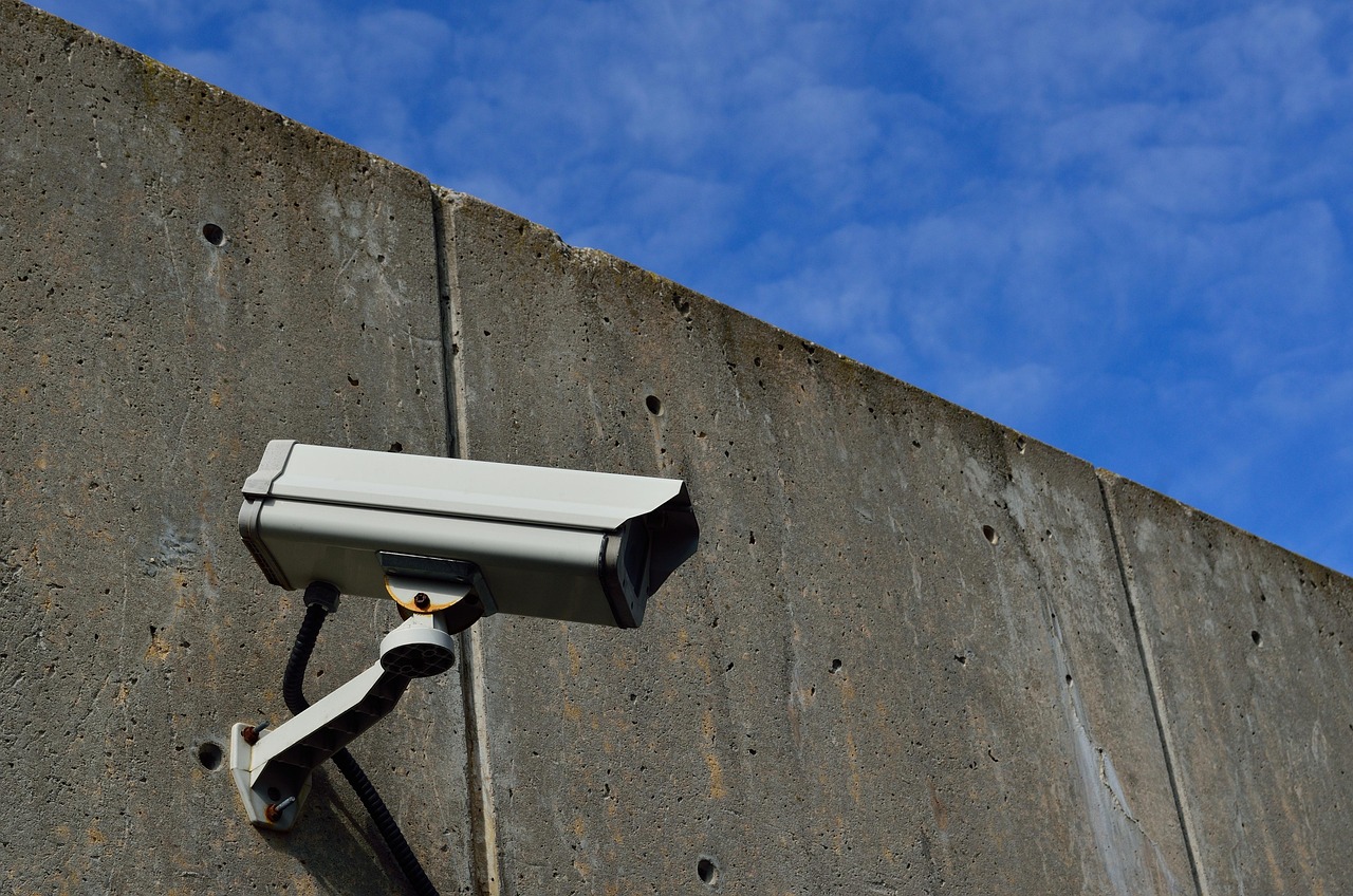 A single box CCTV camera on an articulated bracket, fixed to a bare concrete wall against a blue sky. The hardware is bought once; what it remembers is billed monthly.