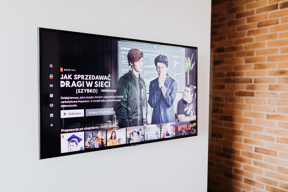 A flat-screen television mounted on a white wall beside exposed orange brickwork, showing a streaming service home page in Polish