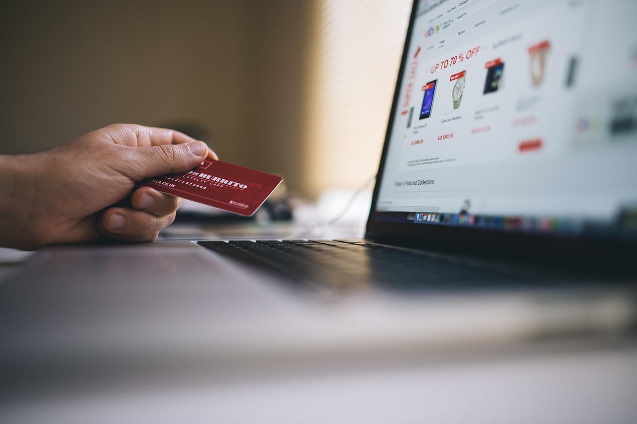 Una mano che tiene una carta rossa accanto a un portatile che mostra un sito di shopping online