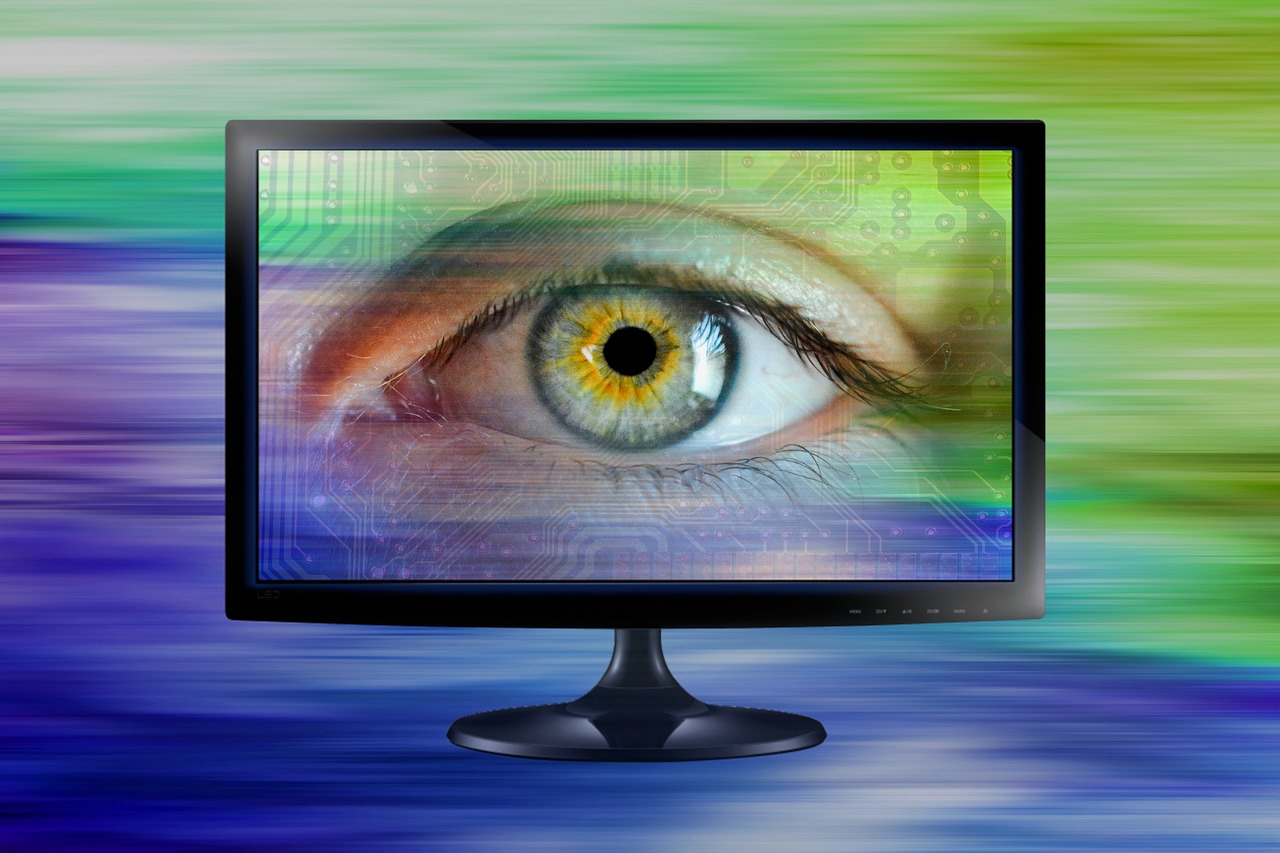 A computer monitor displaying a close-up human eye overlaid with circuit lines, an illustration of digital surveillance