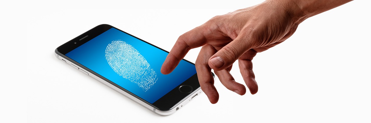 A hand reaching toward a smartphone that shows a glowing fingerprint on a blue screen — biometrics as a second authentication factor.